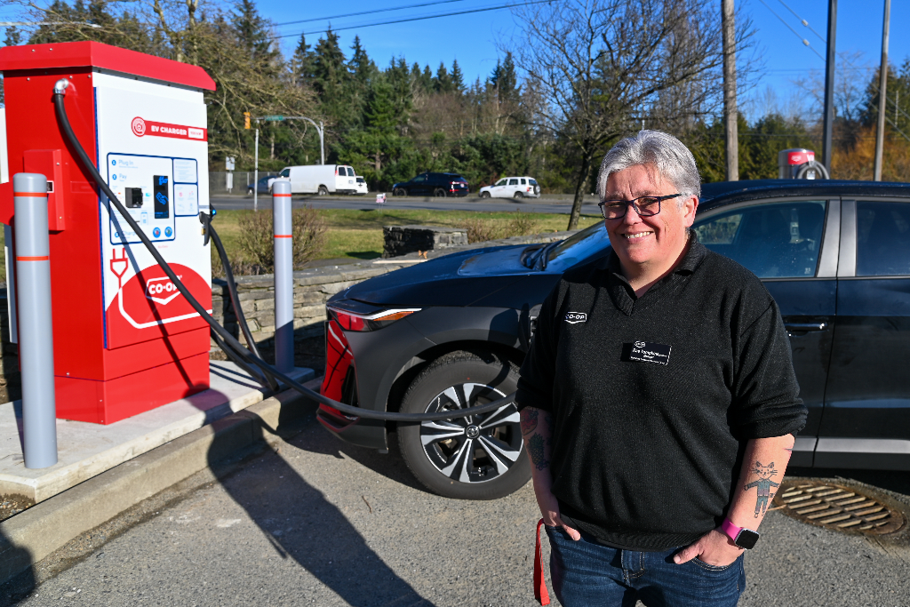 A Co-op gas bar manager stands in front of the new EV charger