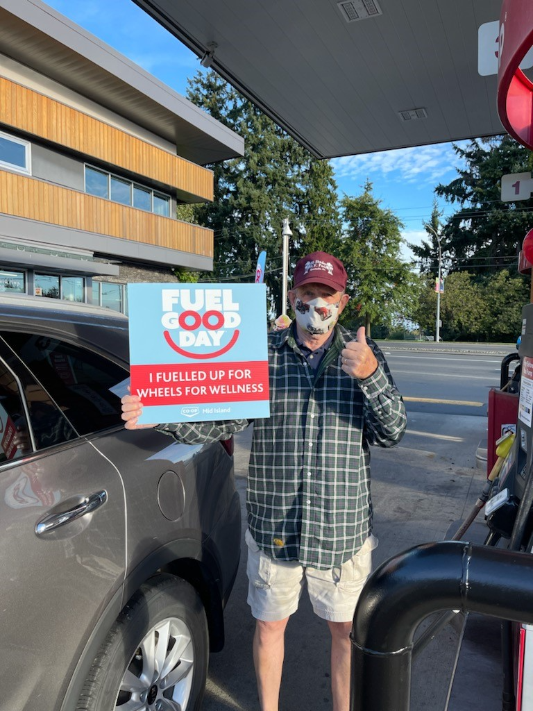 A customer filling us his vehicle with gas holds a Fuel Good Day sign and gives a thumbs up
